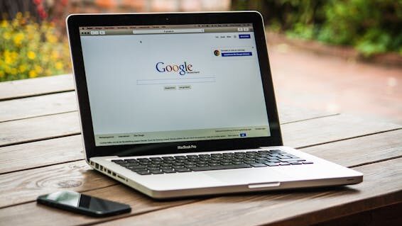 mac-freelancer-macintosh-macbook-40185-40185 A MacBook Pro displaying Google Search on a wooden table outdoors, next to a smartphone.